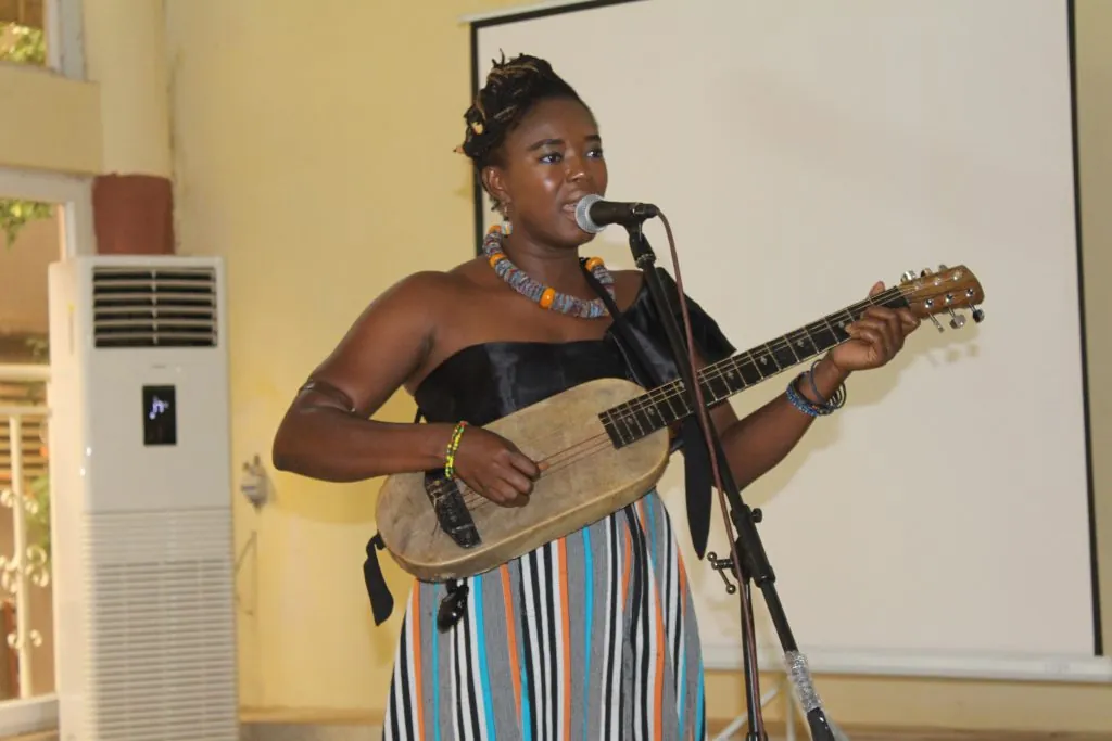 La chanteuse Virginie Dembélé chante au micro en s’accompagnant à la guitare.