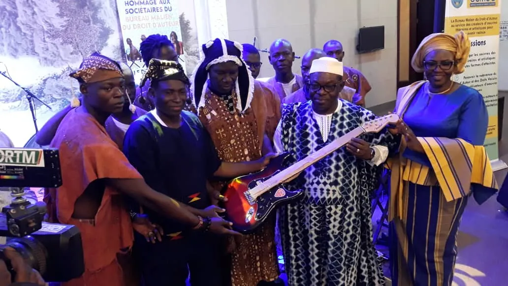 Remise d’une guitare électrique à des musiciens en tenue traditionnelle lors de la cérémonie en hommage aux sociétaires.